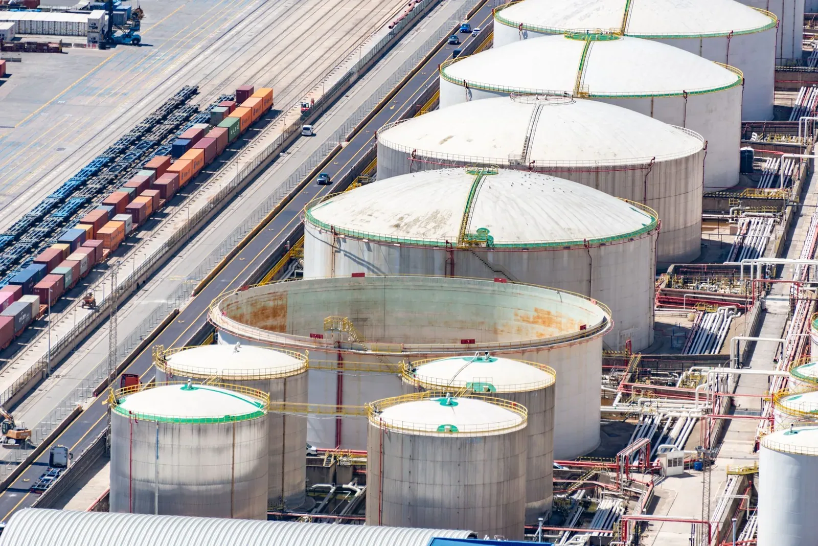 Aerial view of large white oil storage tanks and pipework beside railway tracks and freight wagons in an industrial area
