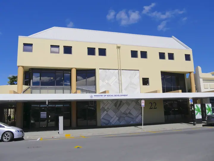 A two-storey cream office building on a sunny street, with a 'Ministry of Social Development' sign above the ground-floor entrance and the number 22 on the facade