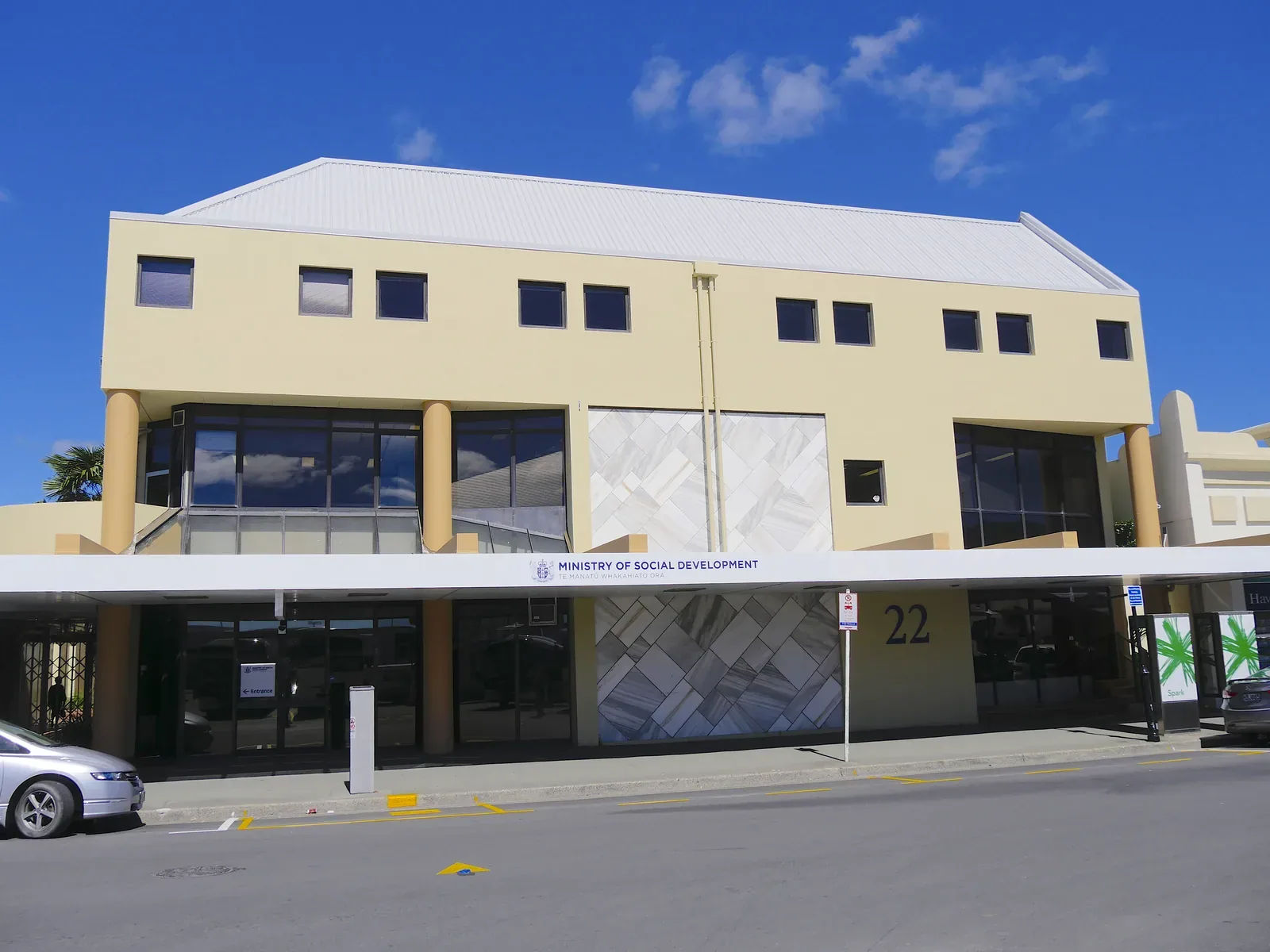 A two-storey cream office building on a sunny street, with a 'Ministry of Social Development' sign above the ground-floor entrance and the number 22 on the facade