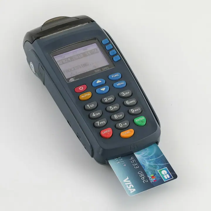 A handheld card payment terminal showing 'Processing' on its screen, with a Visa card inserted in the reader slot