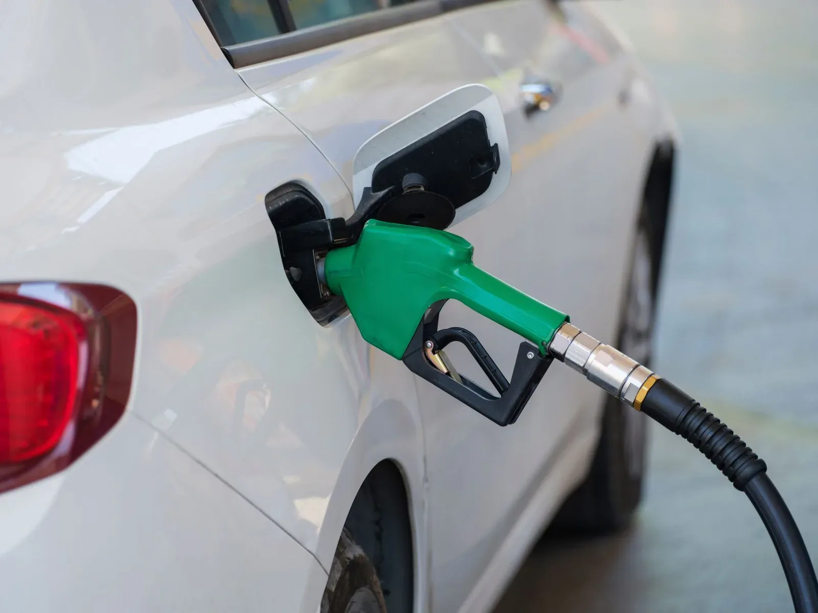 A green fuel nozzle inserted in the open fuel filler of a white car at a petrol station
