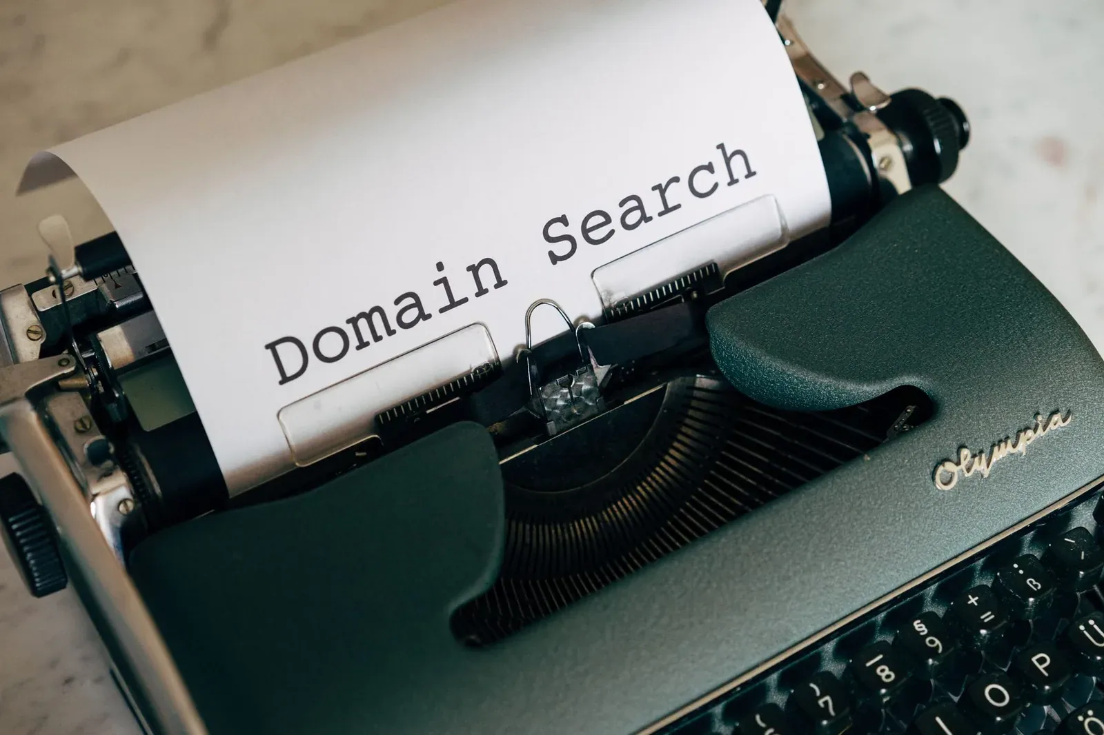 Close-up of a dark green vintage typewriter with a sheet of paper reading "Domain Search"