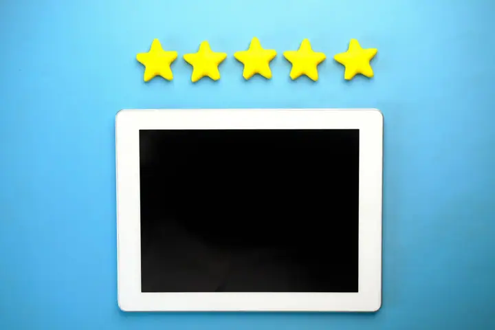 A white tablet with a blank screen lying on a blue surface beneath a row of five yellow stars