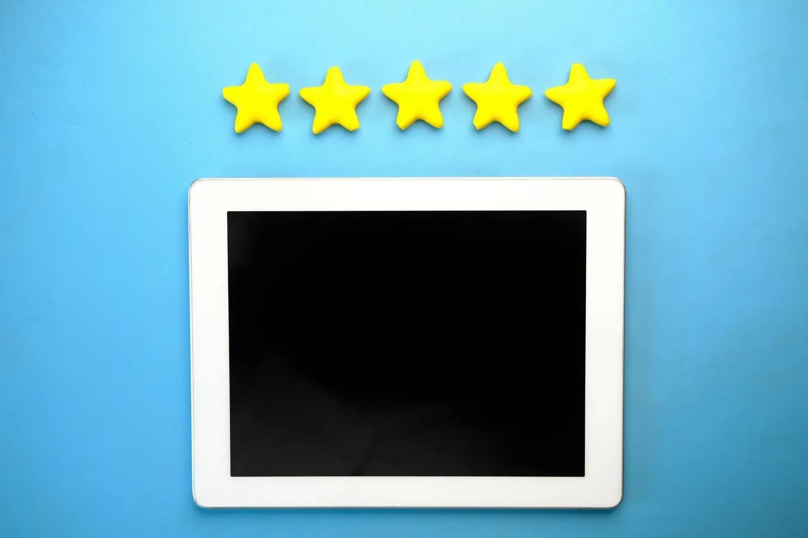 A white tablet with a blank screen lying on a blue surface beneath a row of five yellow stars