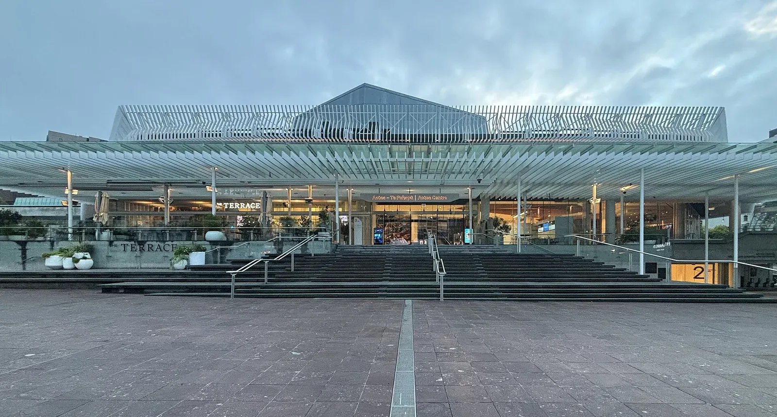 The glass-fronted Aotea Centre seen across an empty Aotea Square at dusk, with wide steps leading up under a long white canopy