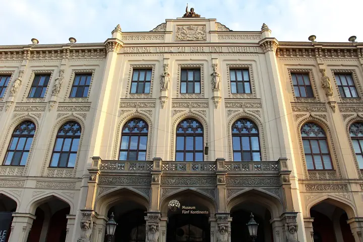 Ornate cream-coloured neoclassical facade of a museum building, with arched windows, statues in niches and a sign reading "Museum Fünf Kontinente" above the central entrance