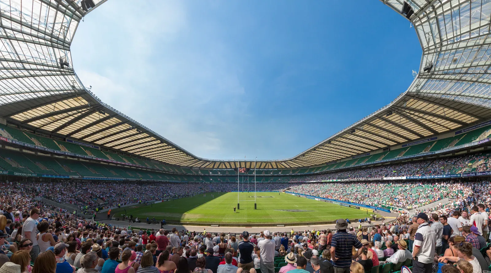 Panoramic view from the stands inside Twickenham Stadium, packed with spectators, looking across the rugby pitch under a blue sky