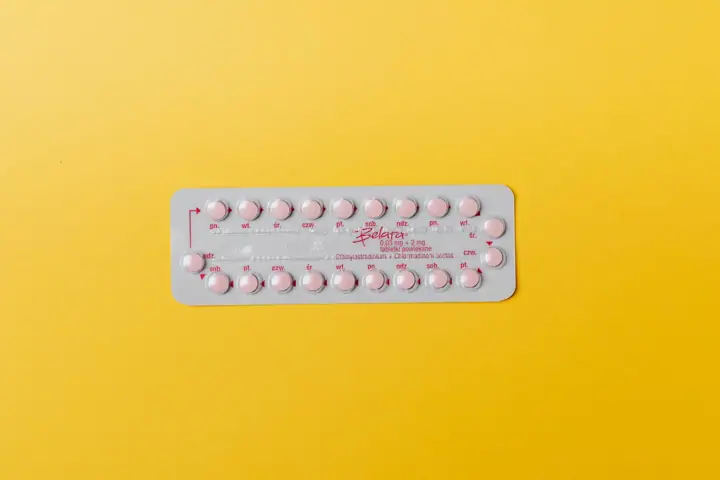 A blister pack of small pink pills laid on a bright yellow background