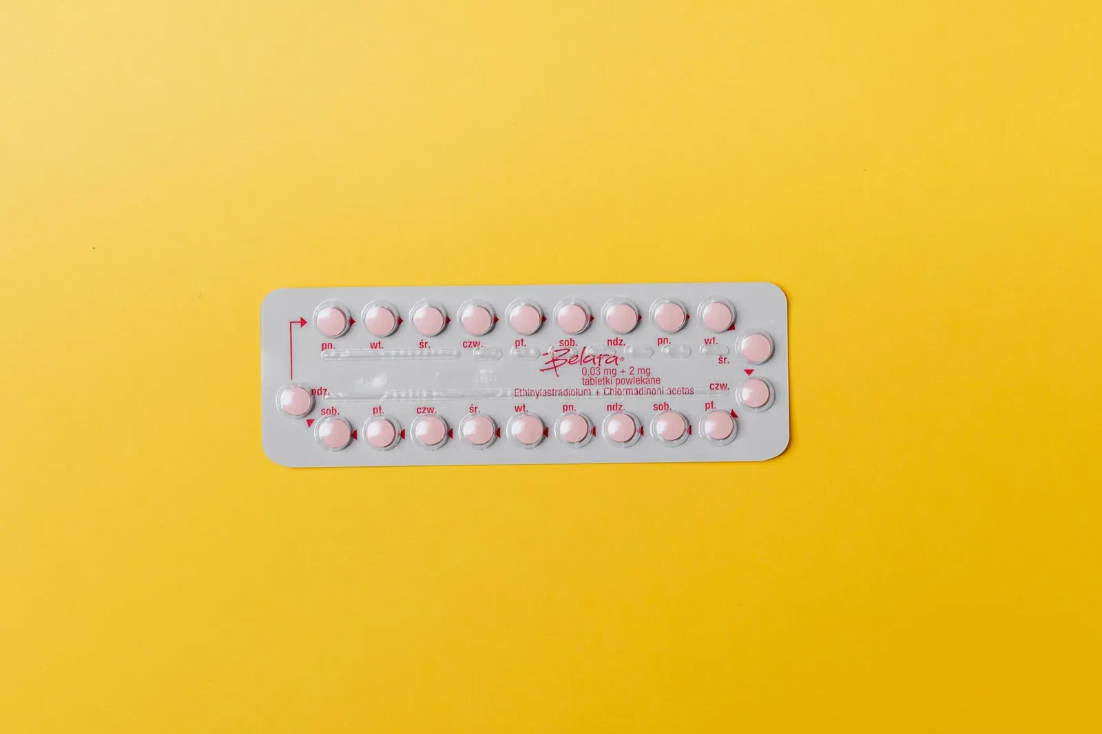 A blister pack of small pink pills laid on a bright yellow background