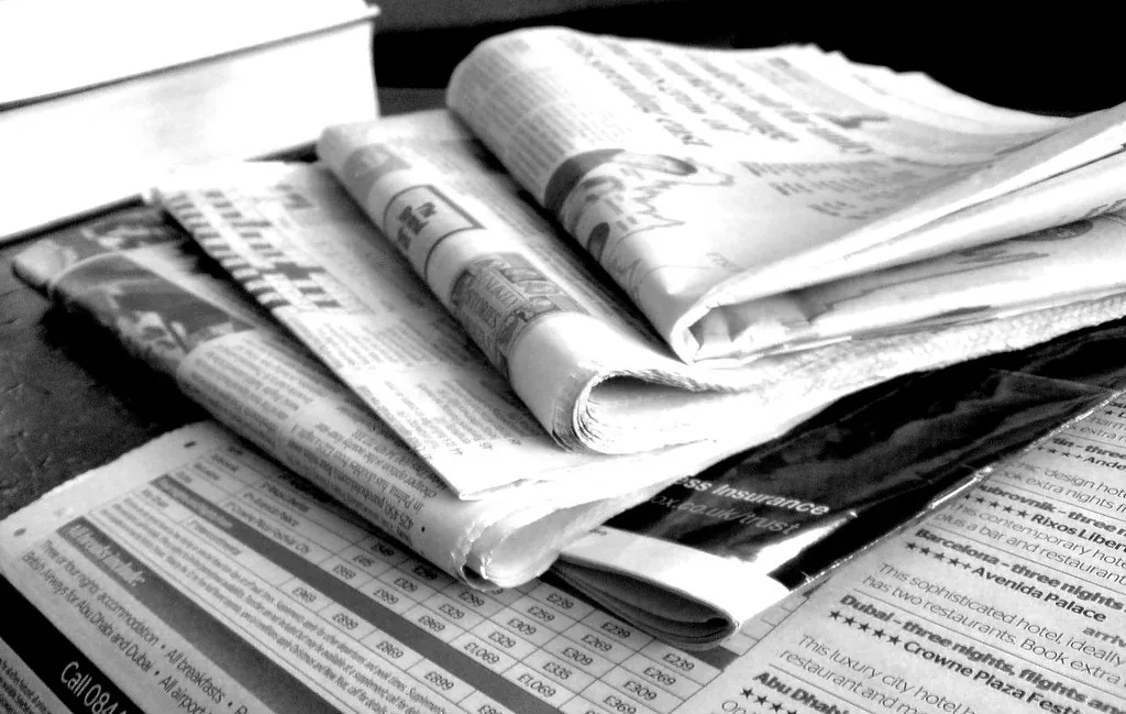 Black-and-white close-up of a pile of folded newspapers on a table
