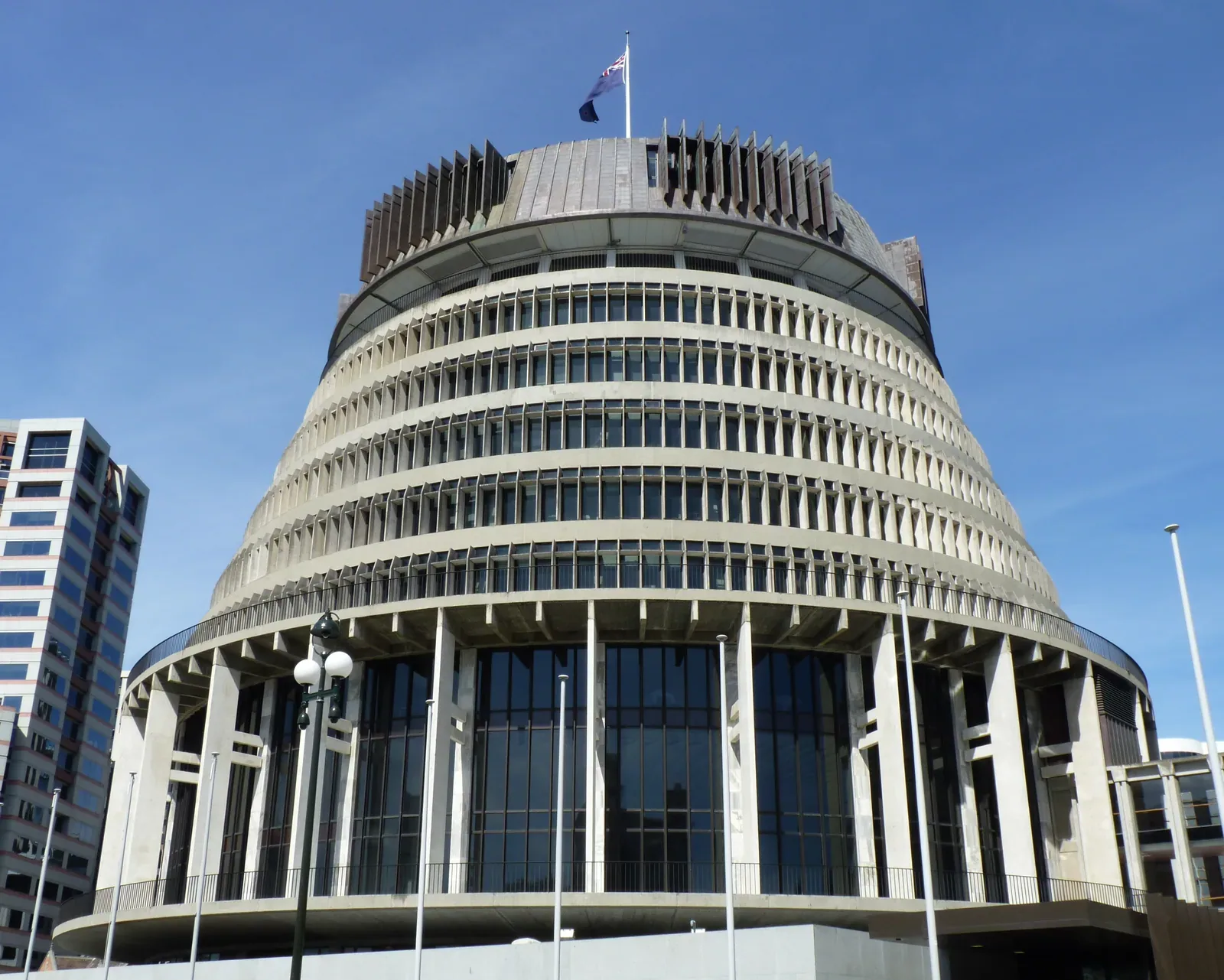The round, tiered Beehive building in Wellington under a clear blue sky, with the New Zealand flag flying from its roof