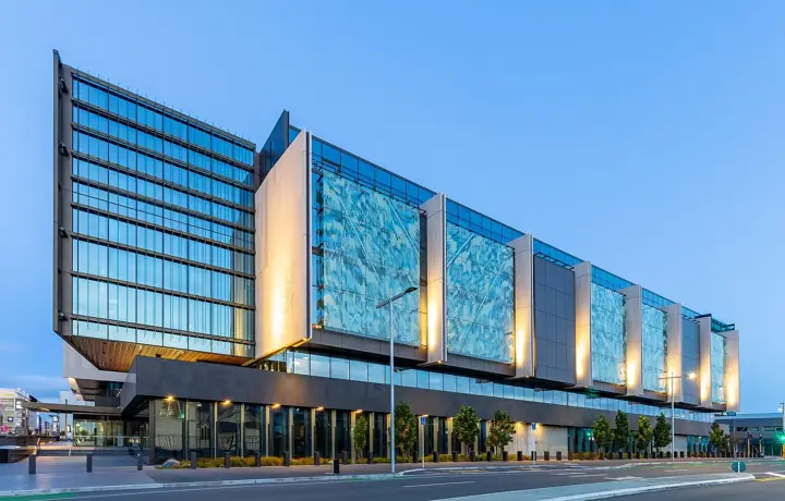 A modern multi-storey courts building with glass facades and illuminated patterned panels, photographed at dusk against a deep blue sky