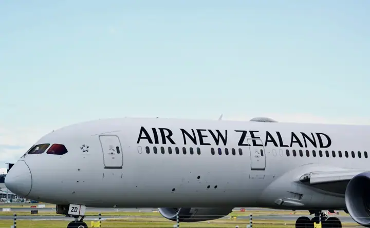 A white Air New Zealand Boeing 787 Dreamliner with 'AIR NEW ZEALAND' in large black letters on the fuselage, on the tarmac