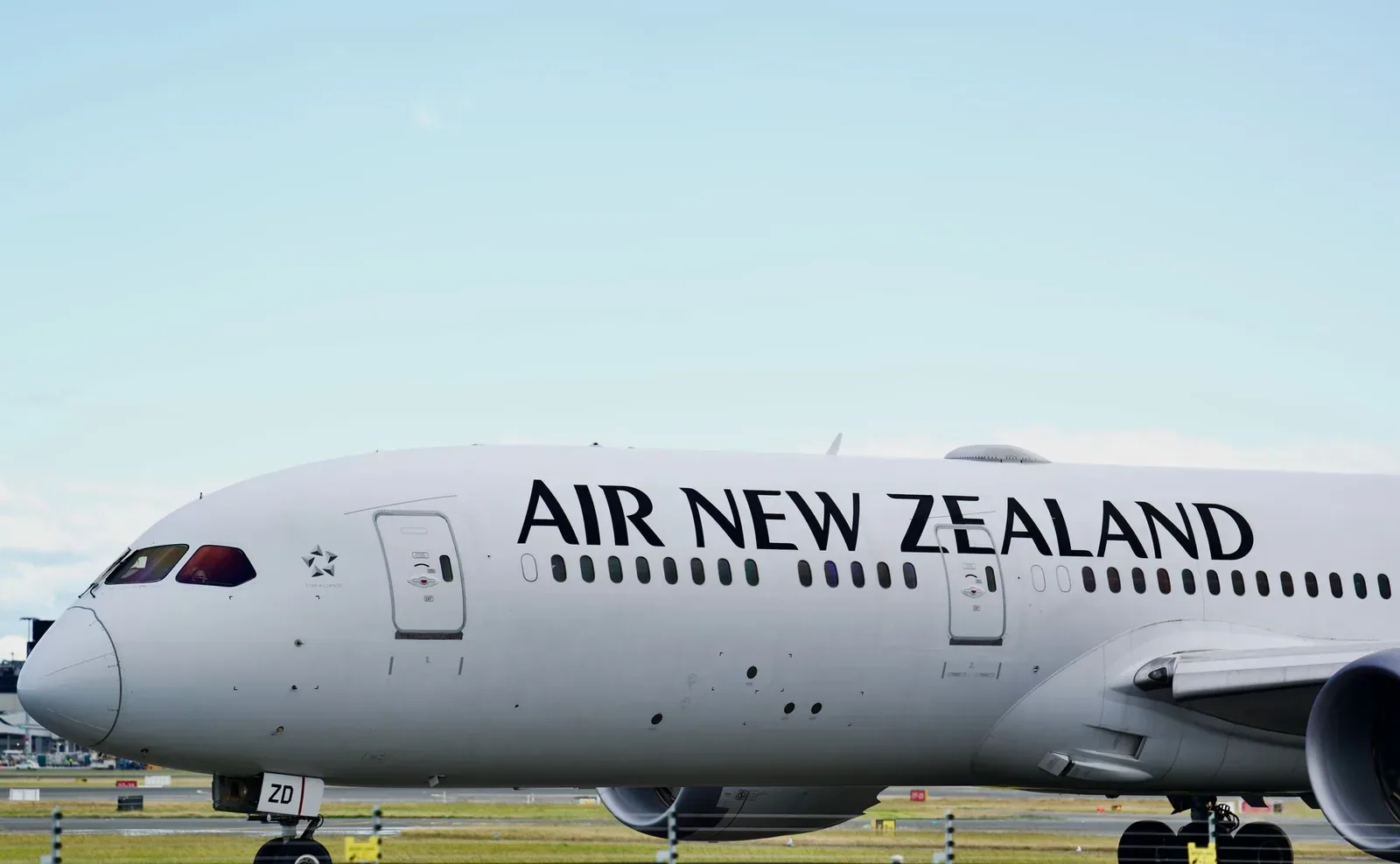 A white Air New Zealand Boeing 787 Dreamliner with 'AIR NEW ZEALAND' in large black letters on the fuselage, on the tarmac