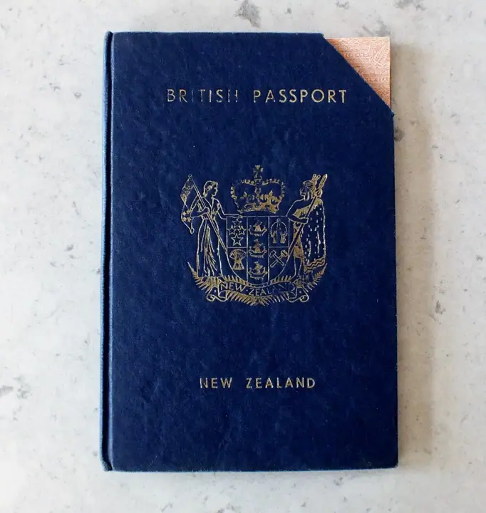 Dark blue hardback passport cover with gold lettering reading 'British Passport' and 'New Zealand' around the New Zealand coat of arms, lying on a pale stone surface