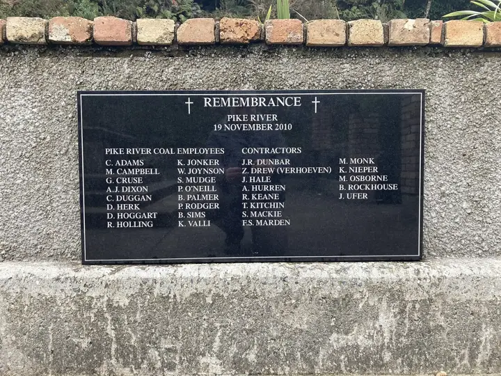 A black stone plaque set into a concrete wall, headed 'Remembrance – Pike River – 19 November 2010', listing the names of Pike River Coal employees and contractors.