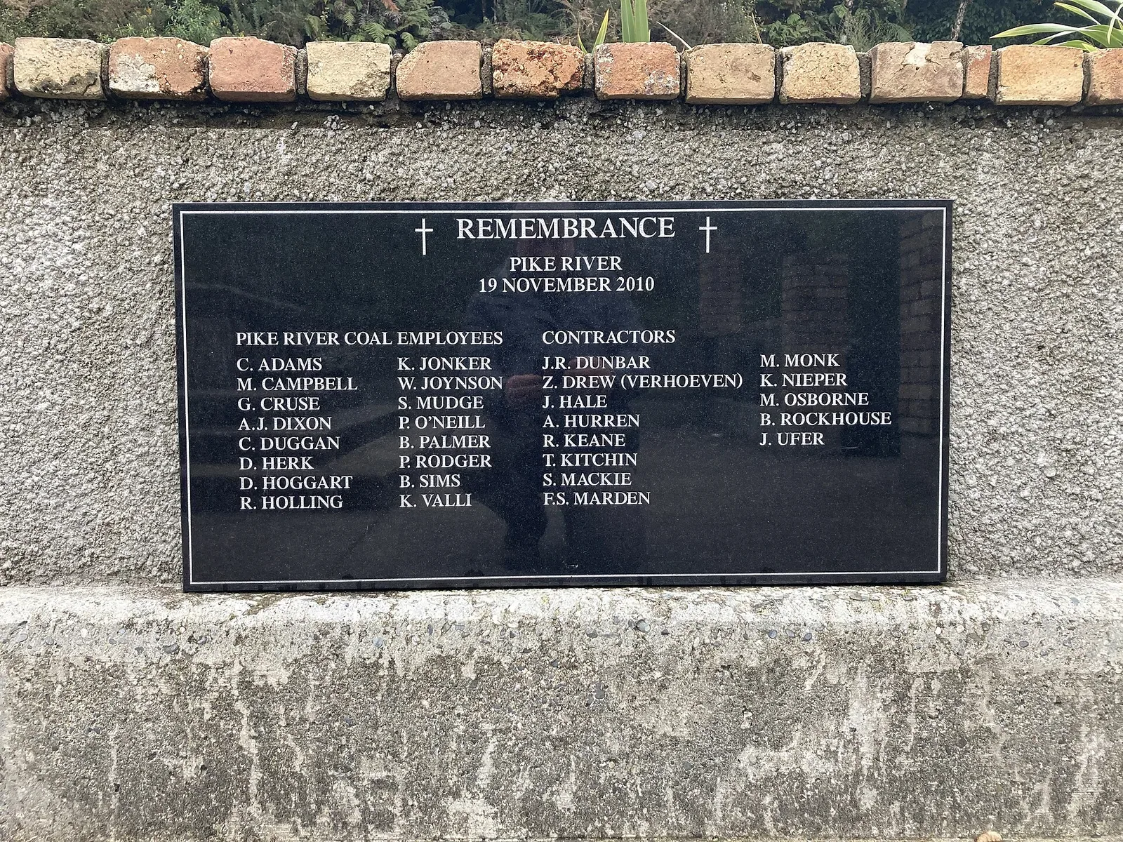 A black stone plaque set into a concrete wall, headed 'Remembrance – Pike River – 19 November 2010', listing the names of Pike River Coal employees and contractors.