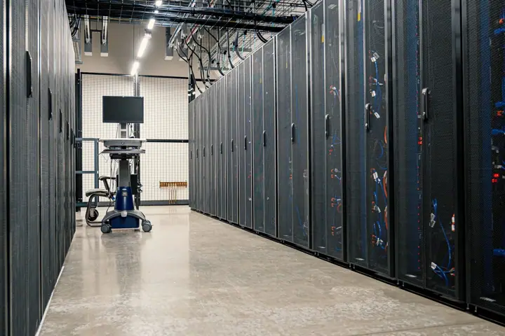 A row of black steel server cabinets filled with networking equipment and cables along a corridor in a data centre