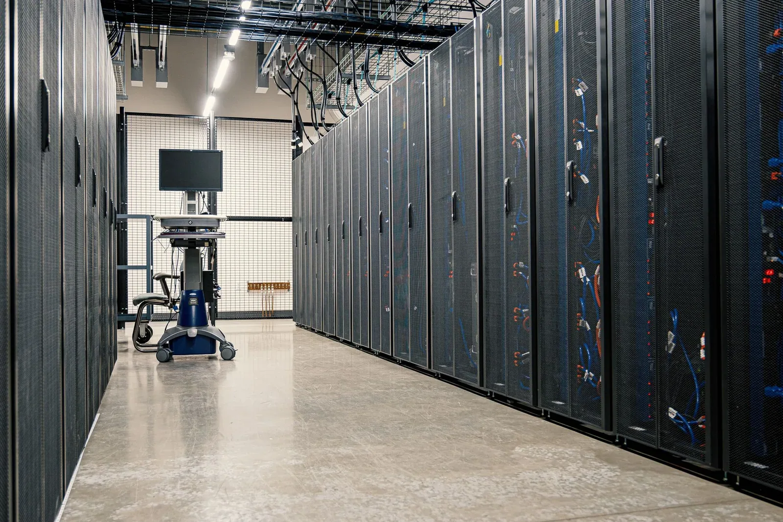 A row of black steel server cabinets filled with networking equipment and cables along a corridor in a data centre