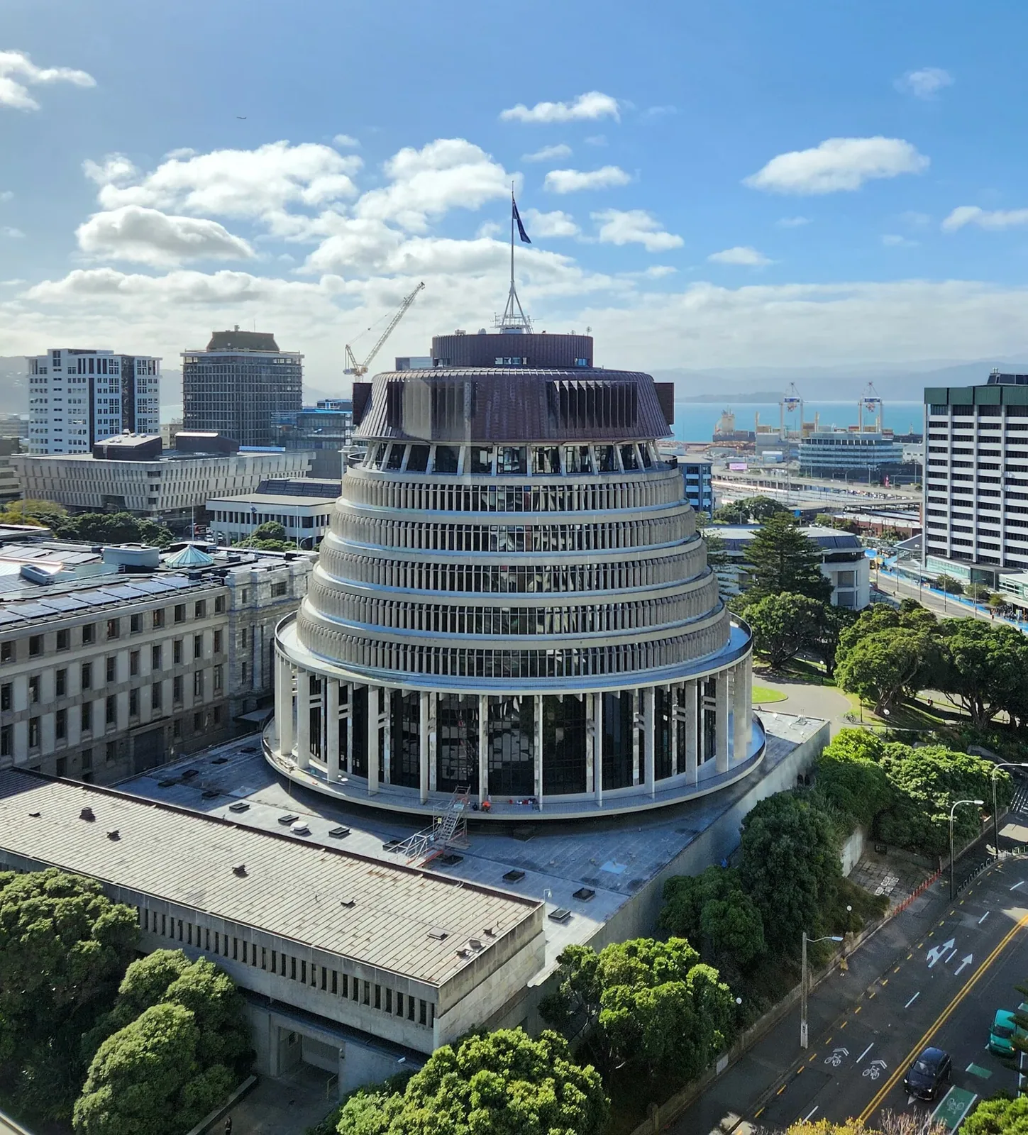 Elevated view of the Beehive, the round tiered government building in Wellington, with the New Zealand flag flying on top and the city and harbour behind